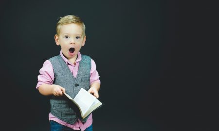 boy wearing gray vest and pink dress shirt holding book