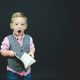 boy wearing gray vest and pink dress shirt holding book