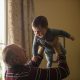 man wearing maroon, white, and blue stripe long-sleeved shirt lifting up baby wearing gray onesie