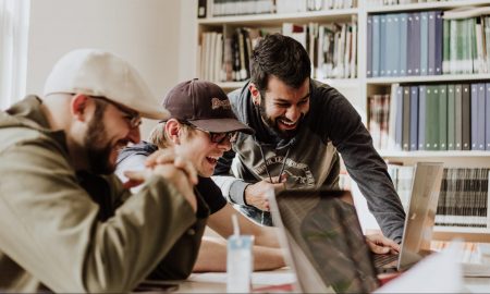 three men laughing while looking in the laptop inside room