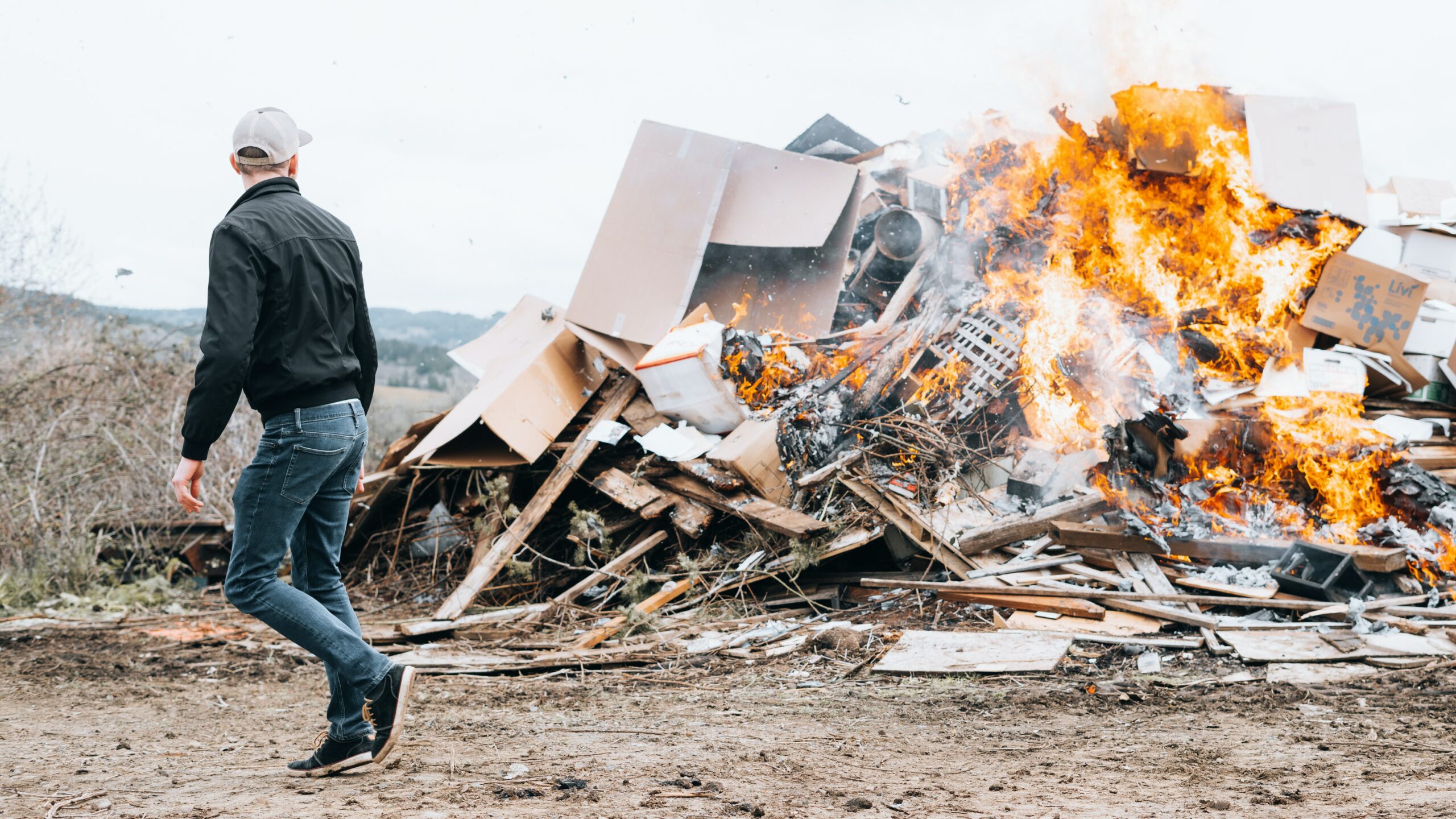 man in black jacket and blue denim jeans standing in front of bonfire