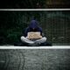 man in blue hoodie reading book on gray concrete road during daytime