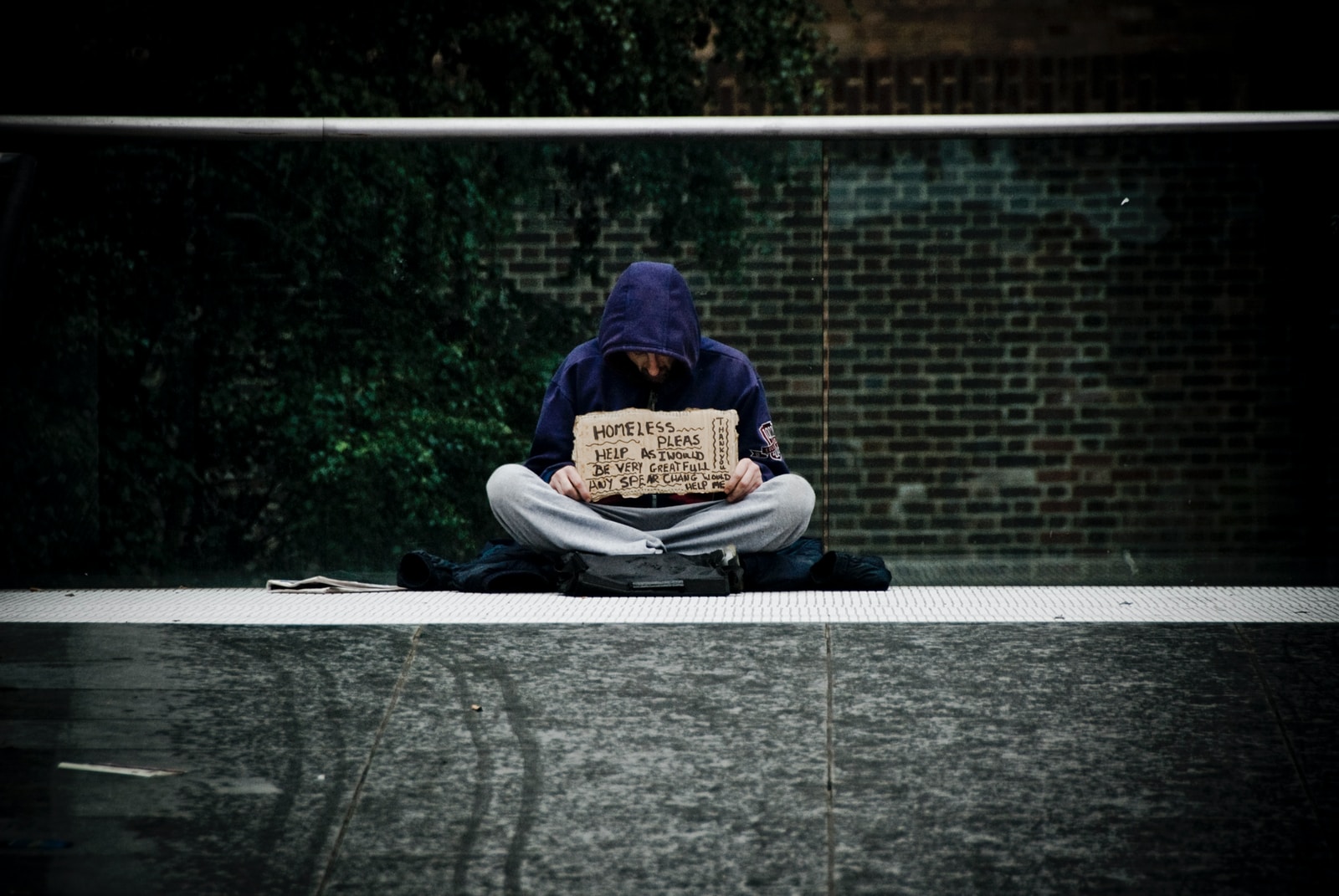 man in blue hoodie reading book on gray concrete road during daytime