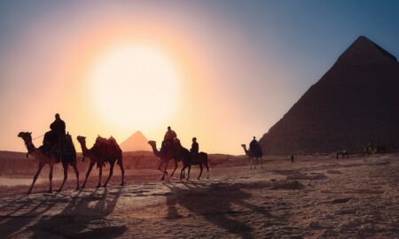 five persons riding camels walking on sand beside Pyramid of Egypt