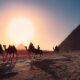 five persons riding camels walking on sand beside Pyramid of Egypt