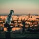 selective focus photography of telescope by cityscape during daytime