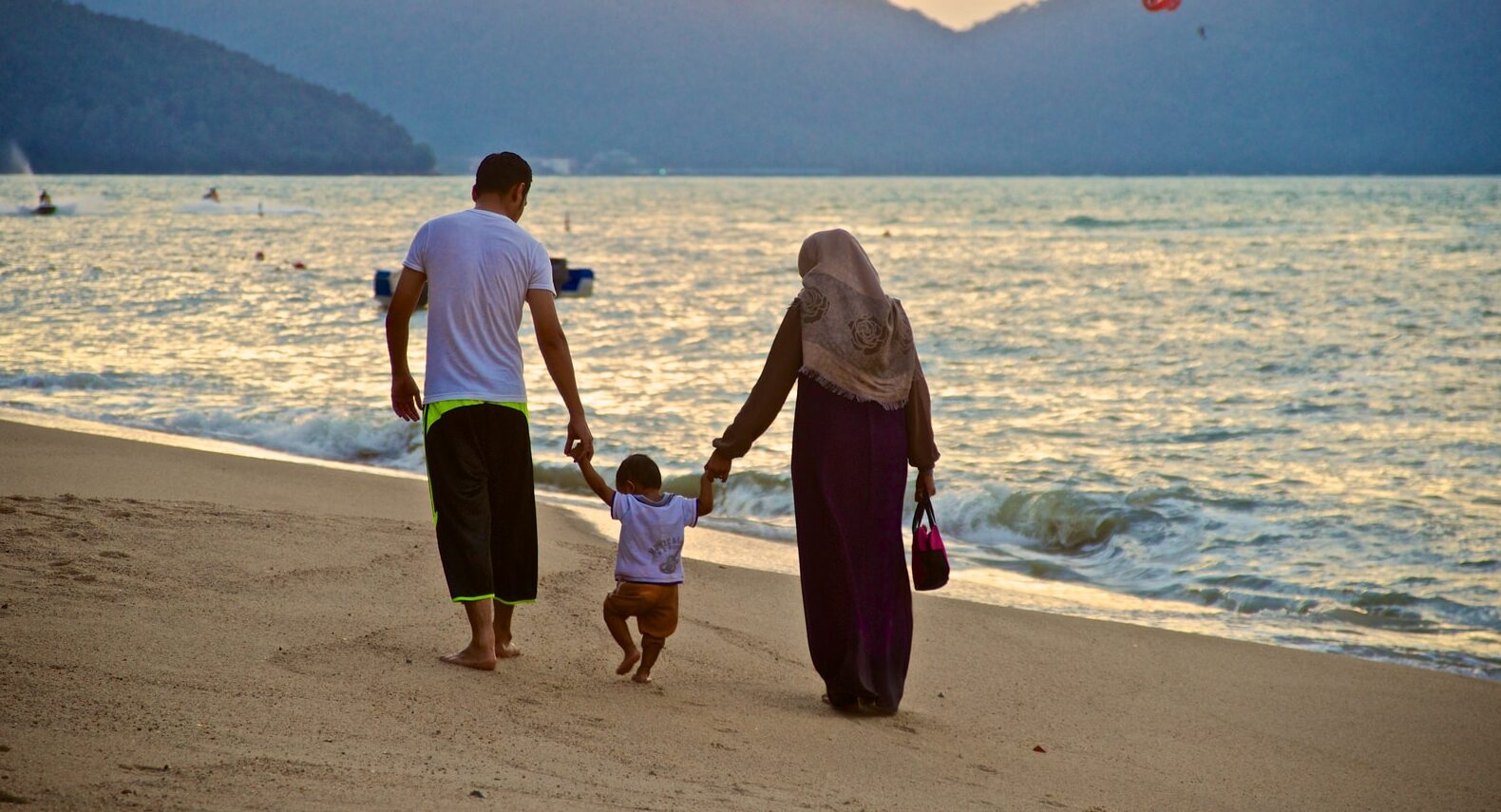 man and woman holding hands while walking on beach during daytime