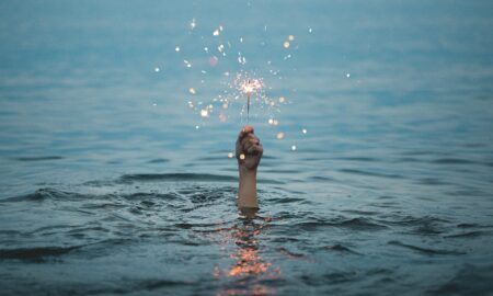 person submerged on body of water holding sparkler