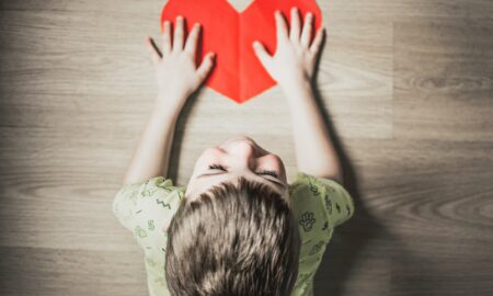 boy in green shirt holding red paper heart cutout on brown table