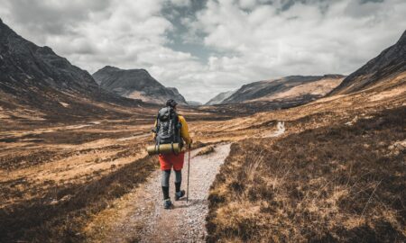 person wearing backpack walking on dirt road