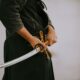 person in black long sleeve shirt and black skirt holding white leather belt