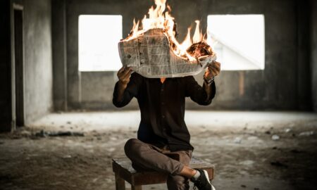 man sitting on chair holding newspaper on fire