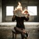 man sitting on chair holding newspaper on fire