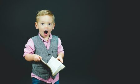 boy wearing gray vest and pink dress shirt holding book