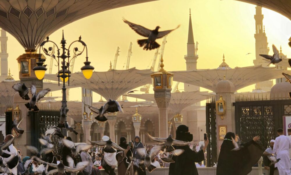 Captivating view of Al-Masjid an-Nabawi at sunset with pigeons in flight, symbolizing peace.
